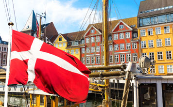Denmark's national flag flying in the foreground of Copenhagen's famous old Nyhavn port.