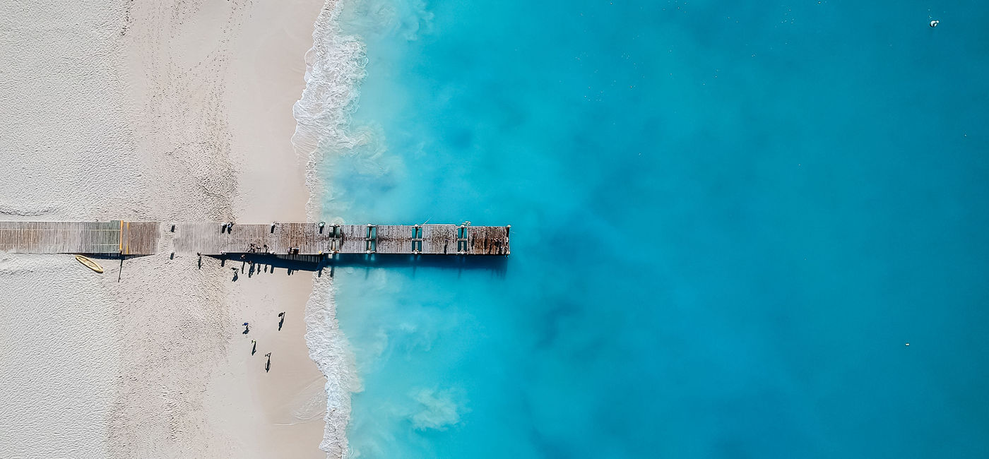 Image: Drone photo of pier in Grace Bay, Providenciales, Turks and Caicos. The caribbean blue sea and white sandy beaches can be seen (photo via JoaoBarcelos / iStock / Getty Images Plus)
