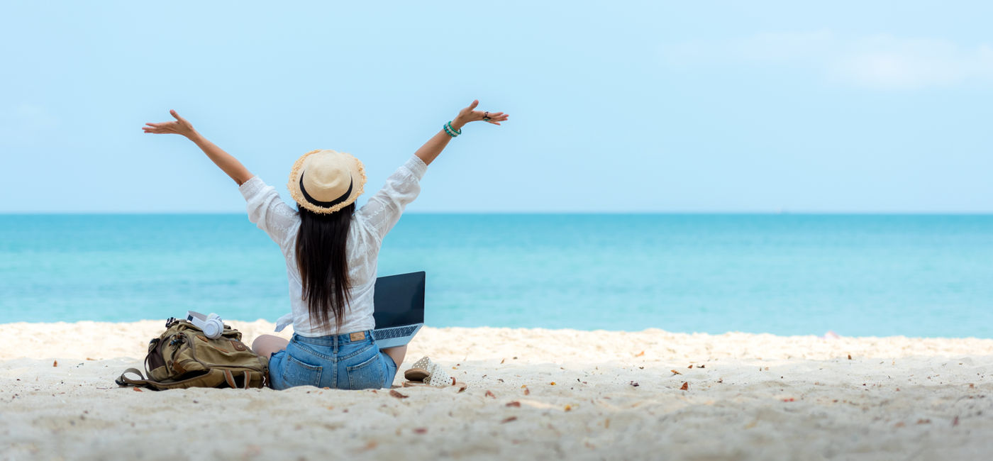 Image: Female traveler on the beach working on laptop (Photo Credit: Adobe Stock / freebird7977)