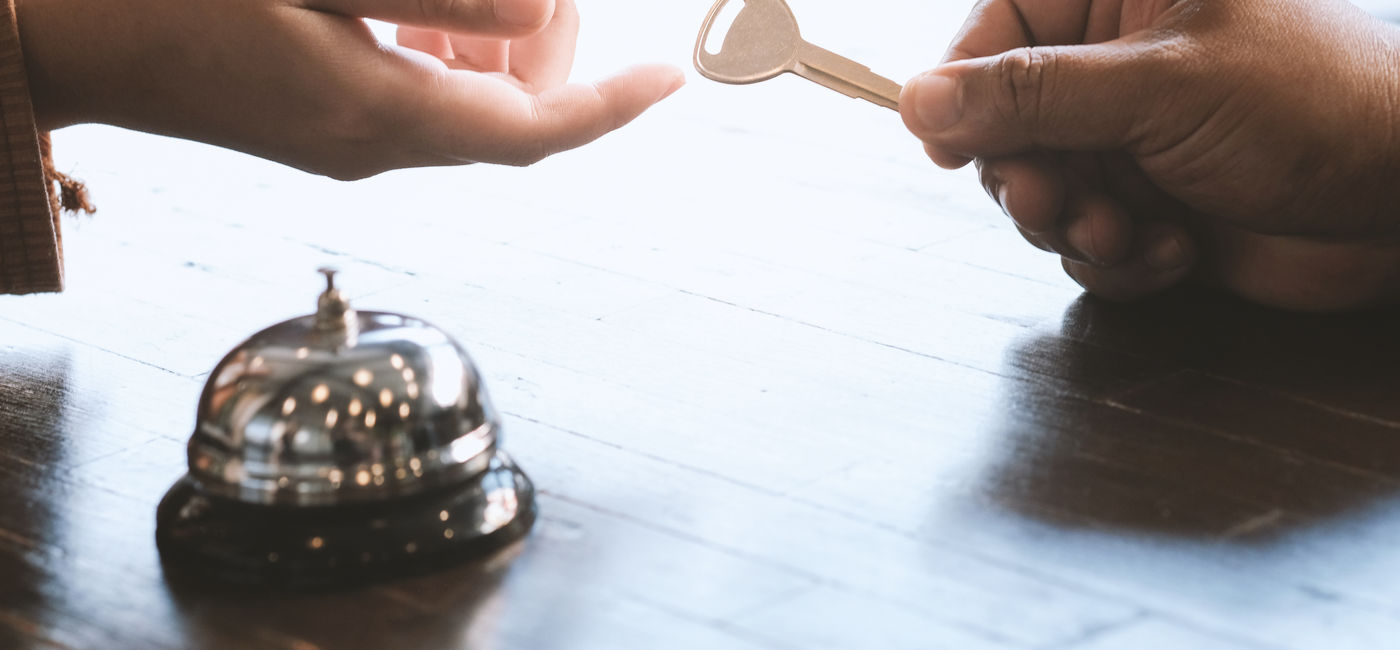 Image: Guest checking in at a hotel front desk. (Photo Credit: Adobe Stock/Charlie's)