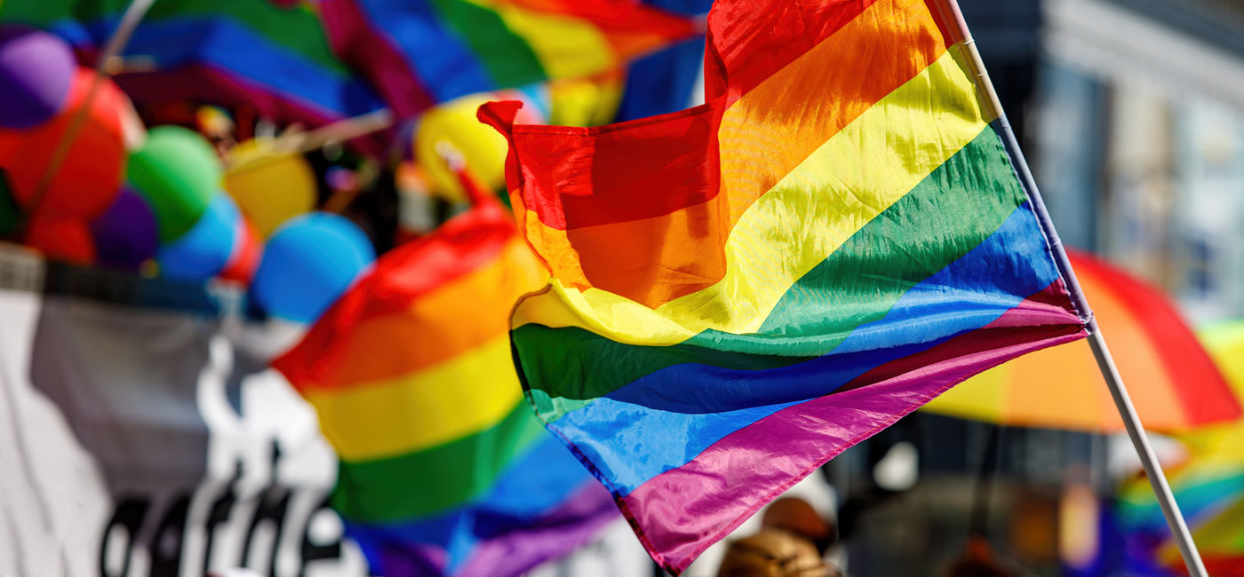 Image: LGBTQI+ flag being waved at a pride parade. (Photo Credit: Adobe Stock/9parusnikov)