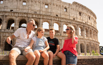 A family of travelers sits in front of the Colosseum in Rome, Italy.