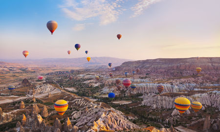 Hot air balloon flying over rock landscape at Cappadocia Turkey (photo via TPopova / iStock / Getty Images Plus)